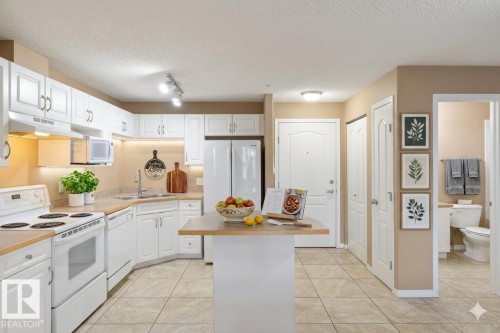 The kitchen features white cabinetry, white appliances, and a central island with a wood-look countertop - 224 3425 19 Street Nw, Edmonton, AB - Indoor Photo Showing Kitchen With Double Sink