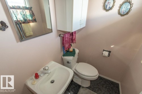 This bathroom features a white sink with a faucet, a toilet, a mirror, and white wall-mounted cabinetry - 5013 45 St, St. Paul Town, AB - Indoor Photo Showing Bathroom