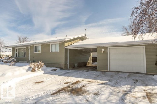 The property features a light-colored exterior, a white garage door, and a covered carport area - 5013 45 St, St. Paul Town, AB - Outdoor