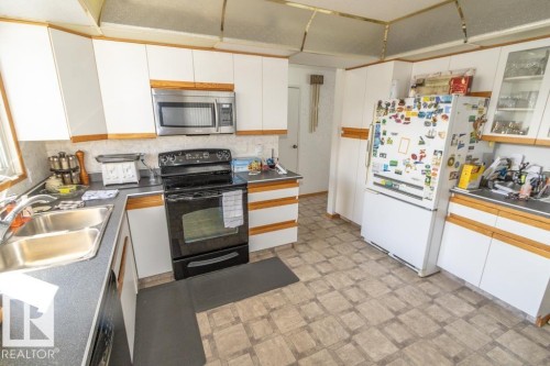 The kitchen features white cabinetry with wood trim, a double basin stainless steel sink, a black range, and a stainless steel microwave - 5013 45 St, St. Paul Town, AB - Indoor Photo Showing Kitchen With Double Sink