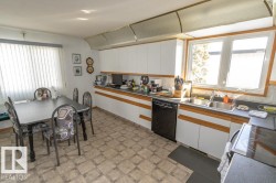 The kitchen features ample white cabinetry with wood trim, a double stainless steel sink, and a black dishwasher - 