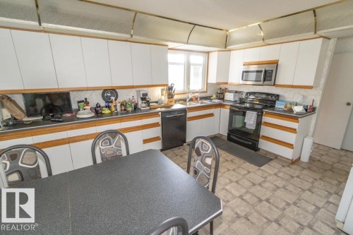 The kitchen features white cabinetry with wood trim, a double basin stainless steel sink, a microwave, and an electric range - 5013 45 St, St. Paul Town, AB - Indoor Photo Showing Kitchen