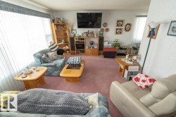 Living area featuring a soft pink carpet, ample natural light from large windows, and a built-in media console with storage - 