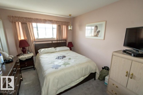 The bedroom features a window with curtains, a bed with a headboard, and soft carpeted flooring - 5013 45 St, St. Paul Town, AB - Indoor Photo Showing Bedroom