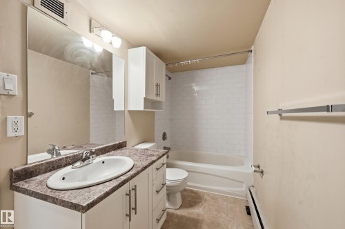 Bathroom featuring a vanity with a white basin and a speckled countertop, a large mirror, and a shower with white subway tile surround - 209 9710 105 Street Nw, Edmonton, AB - Indoor Photo Showing Bathroom