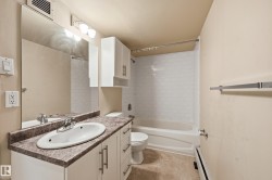 Bathroom featuring a vanity with a white basin and a speckled countertop, a large mirror, and a shower with white subway tile surround - 