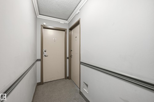 This photo captures a hallway with light-colored walls and crown molding - 209 9710 105 Street Nw, Edmonton, AB - Indoor Photo Showing Other Room