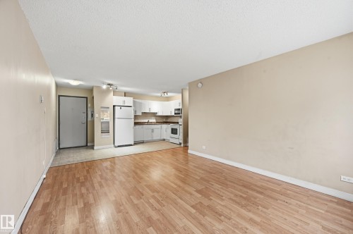 The property features light-toned walls and wood-style flooring in the living area, with a kitchen visible in the background - 209 9710 105 Street Nw, Edmonton, AB - Indoor