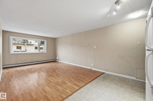 The open-concept living area features a mix of wood-style flooring and tiled flooring, with a window providing outdoor views - 209 9710 105 Street Nw, Edmonton, AB - Indoor Photo Showing Other Room