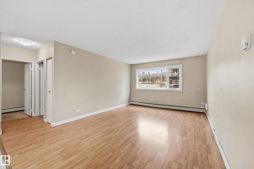 This bright living area features light-toned walls and wood-style flooring, complemented by a large window that offers views of the exterior - 209 9710 105 Street Nw, Edmonton, AB - Indoor