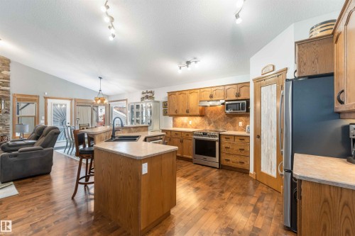 The kitchen features wood cabinetry, stainless steel appliances, a center island with a sink, and hardwood flooring throughout - 61 Linkside Blvd, Spruce Grove, AB - Indoor Photo Showing Kitchen With Double Sink