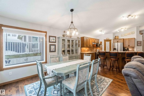 The open concept living area features hardwood floors, a dining area with a chandelier, and a kitchen with wooden cabinetry, stainless steel appliances, and a breakfast bar with seating - 61 Linkside Blvd, Spruce Grove, AB - Indoor Photo Showing Dining Room
