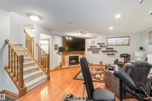 The property features a spacious living area with hardwood flooring, a fireplace with a wooden mantel, and a staircase with carpeted treads and wooden handrails - 61 Linkside Blvd, Spruce Grove, AB - Indoor With Fireplace