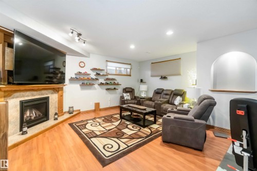 The living area features warm wood flooring, a fireplace with a stone surround, and an arched wall niche - 61 Linkside Blvd, Spruce Grove, AB - Indoor Photo Showing Living Room With Fireplace