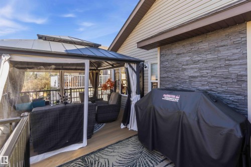 Outdoor patio featuring a covered gazebo with screens, composite decking, and a stone accent wall - 61 Linkside Blvd, Spruce Grove, AB - Outdoor With Deck Patio Veranda