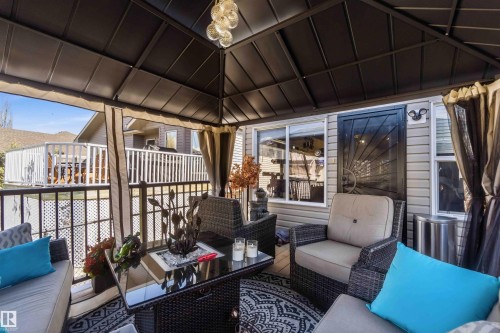 Covered patio area featuring a dark gazebo structure, a decorative metal security door, and light-colored siding - 61 Linkside Blvd, Spruce Grove, AB - Outdoor With Deck Patio Veranda With Exterior