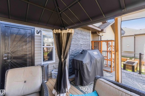 Covered outdoor patio featuring composite wood-finish decking, a privacy screen, and a stone accent wall - 61 Linkside Blvd, Spruce Grove, AB -  With Exterior
