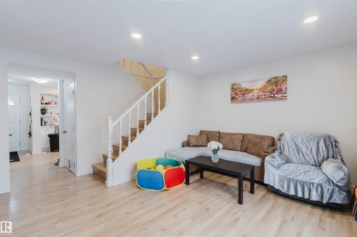 This bright living area features light-toned flooring, a staircase with white railings, and recessed ceiling lights - 18088 93 Avenue Nw, Edmonton, AB - Indoor Photo Showing Living Room