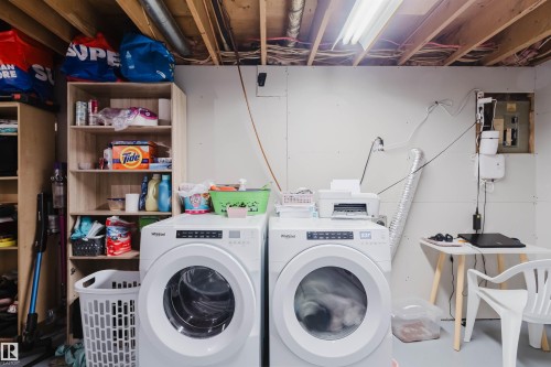 Laundry area featuring two front-loading machines, built-in shelving, and a utility table - 18088 93 Avenue Nw, Edmonton, AB - Indoor Photo Showing Laundry Room