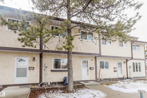 The property presents a facade with light-colored stucco and siding, featuring multiple windows and individual entrances - 18088 93 Avenue Nw, Edmonton, AB - Outdoor