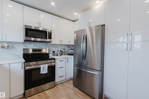 The kitchen features white cabinetry with stainless steel appliances, including a microwave, range, and refrigerator - 18088 93 Avenue Nw, Edmonton, AB - Indoor Photo Showing Kitchen With Upgraded Kitchen