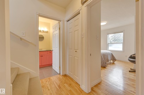 This interior hallway features hardwood flooring, a closed closet, and provides access to a bathroom with a red vanity and a room with a large window - 10940 71 Avenue, Edmonton, AB - Indoor Photo Showing Other Room