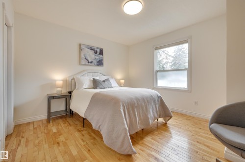 This room features light-toned hardwood flooring, a window offering natural light, and a ceiling-mounted light fixture - 10940 71 Avenue, Edmonton, AB - Indoor Photo Showing Bedroom