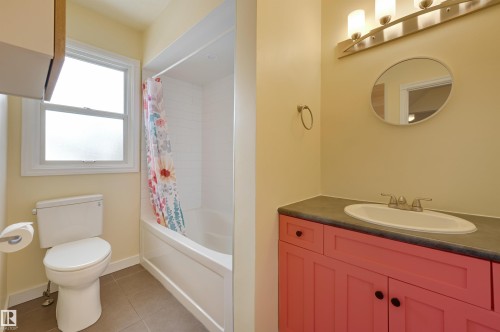 The bathroom features a vibrant vanity with a countertop and an integrated sink, complemented by an oval mirror and modern lighting fixtures - 10940 71 Avenue, Edmonton, AB - Indoor Photo Showing Bathroom