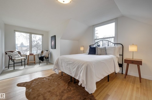 This property features light-colored hardwood flooring, a large window providing natural light, and sloped ceilings - 10940 71 Avenue, Edmonton, AB - Indoor Photo Showing Bedroom