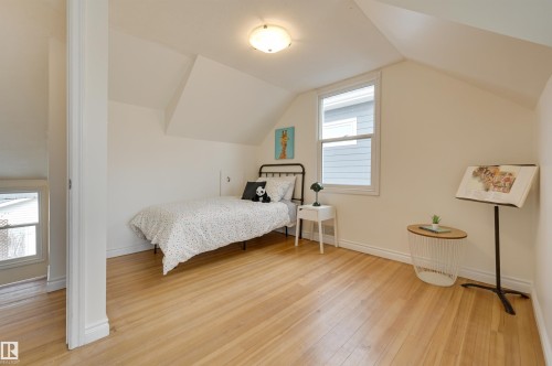 This bright room features light hardwood floors, a window offering natural light, and sloped ceilings - 10940 71 Avenue, Edmonton, AB - Indoor Photo Showing Bedroom
