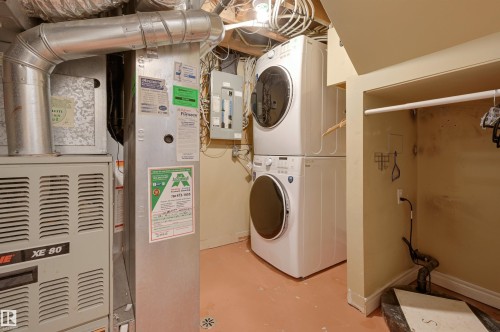 Dedicated laundry area featuring a white stackable washer and dryer, adjacent to the property's furnace and utility systems - 10940 71 Avenue, Edmonton, AB - Indoor Photo Showing Laundry Room
