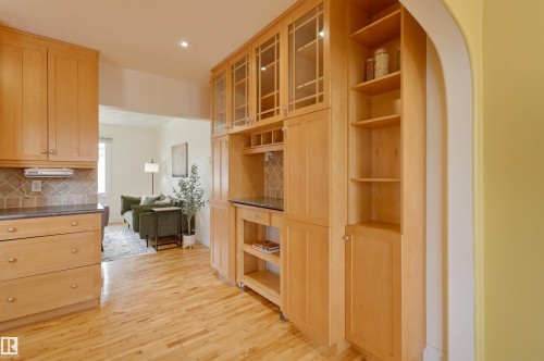 Kitchen featuring light wood cabinetry with glass-front uppers, a tiled backsplash, and light wood flooring - 10940 71 Avenue, Edmonton, AB - Indoor