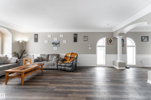 Living area featuring dark wood-style flooring, light gray walls with white wainscoting, and arched windows - 4403 Yeoman Drive, Onoway, AB - Indoor Photo Showing Living Room