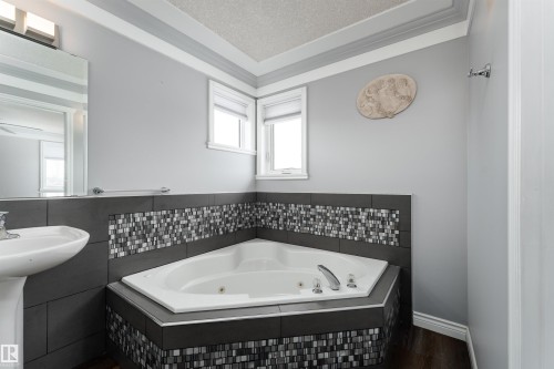 The bathroom features a corner soaking tub with chrome fixtures, a pedestal sink, and a tiled surround with mosaic accents - 4403 Yeoman Drive, Onoway, AB - Indoor Photo Showing Bathroom