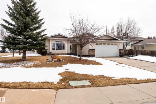 The property features an attached garage with a white door, a paved driveway, and a front yard with mature trees - 4403 Yeoman Drive, Onoway, AB - Outdoor With Facade