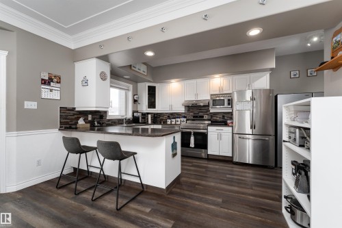 The kitchen features white cabinetry, stainless steel appliances, dark countertops, a tiled backsplash, and dark wood-style flooring - 4403 Yeoman Drive, Onoway, AB - Indoor Photo Showing Kitchen