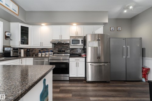 The kitchen features white cabinetry, stainless steel appliances, a mosaic tile backsplash, and dark speckled countertops - 4403 Yeoman Drive, Onoway, AB - Indoor Photo Showing Kitchen