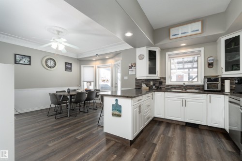 Kitchen and dining area featuring dark wood-style flooring, white cabinetry, a dark countertop, and a dark tile backsplash - 4403 Yeoman Drive, Onoway, AB - Indoor Photo Showing Kitchen
