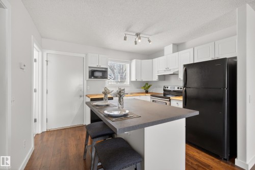 Kitchen featuring dark wood flooring, white cabinetry, a black refrigerator, and an island with a dark countertop - 9 10909 106 Street, Edmonton, AB - Indoor Photo Showing Kitchen