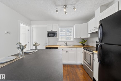 The kitchen features white cabinetry, wood-look countertops, and stainless steel appliances - 9 10909 106 Street, Edmonton, AB - Indoor Photo Showing Kitchen