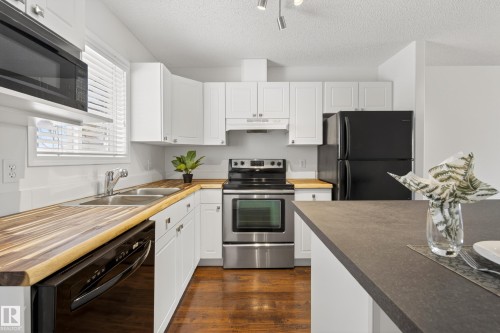 The kitchen features white cabinetry, wood countertops, stainless steel appliances including a range and microwave, and a black refrigerator and dishwasher - 9 10909 106 Street, Edmonton, AB - Indoor Photo Showing Kitchen With Double Sink