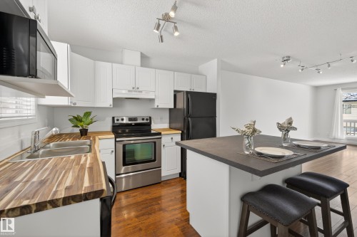 The kitchen features white cabinetry, wooden countertops, stainless steel appliances, and an island with seating - 9 10909 106 Street, Edmonton, AB - Indoor Photo Showing Kitchen With Double Sink