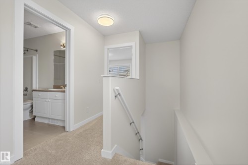 The property features a bright hallway with light-colored carpeting, leading to a bathroom with a white vanity and a toilet - 9 10909 106 Street, Edmonton, AB - Indoor Photo Showing Other Room