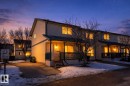 The property features a multi-unit residence with light-colored siding, individual covered porches, and illuminated windows - 9 10909 106 Street, Edmonton, AB  - Outdoor With Deck Patio Veranda 