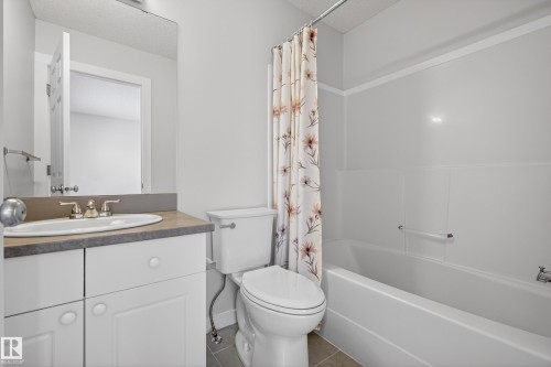 Bathroom featuring a vanity with a white cabinet and a light-colored countertop, a white toilet, and a white bathtub with a shower rod - 9 10909 106 Street, Edmonton, AB - Indoor Photo Showing Bathroom