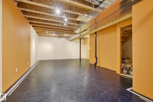 Spacious area featuring exposed ceiling joists, overhead lighting, and walls painted in a warm tone - 9 10909 106 Street, Edmonton, AB - Indoor Photo Showing Basement