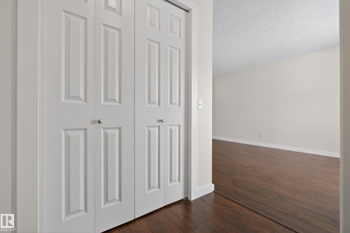 This property features white bi-fold doors with round silver knobs, dark wood flooring, and light-colored walls - 9 10909 106 Street, Edmonton, AB - Indoor Photo Showing Other Room