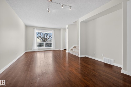 Living area featuring rich hardwood floors, neutral wall paint, and a window with white curtains - 9 10909 106 Street, Edmonton, AB - Indoor
