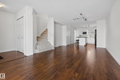 Expansive main living area featuring dark wood flooring, a carpeted staircase, and a kitchen with white cabinetry and a breakfast bar - 9 10909 106 Street, Edmonton, AB - Indoor