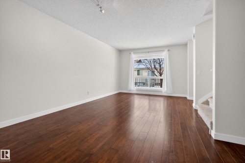 Living area featuring hardwood flooring, light-colored walls, and a window with white curtains - 9 10909 106 Street, Edmonton, AB - Indoor